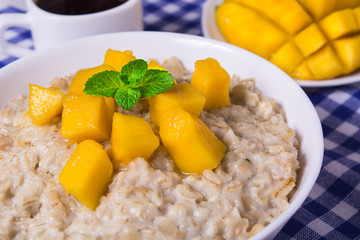 Oat porridge with fresh mango in the white bowl with coffee and book