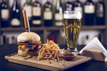 Delicious cheeseburger, tomatoes, and french fries. Beer and napkins on the side. Beautifully served meal at the restaurant. 