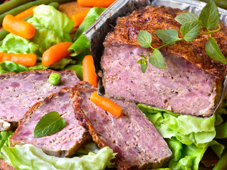 Meatloaf with peas, carrot, lettuce and herbs on a wooden board
