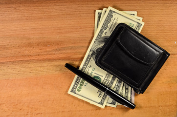 Money clip and one hundred dollars banknotes on wooden table