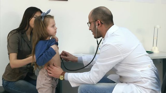 Male pediatrician with stethoscope listening to little girl chest and back