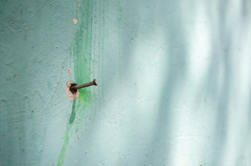 A nail on a green wall. Painting on the wall is peeling off. Selective focus.