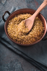 Grain bulgur in a copper bowl and wooden spoon on the slate