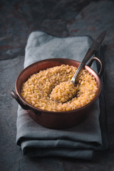 Grain bulgur in a copper bowl and metal spoon on the slate