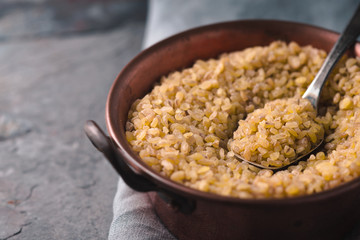 Grain bulgur in a copper bowl and metal spoon on the napkin