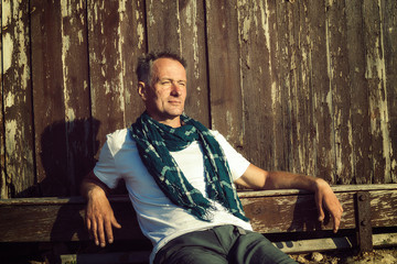 Confident man, traveler sits on the background of a old wooden h