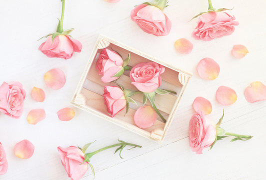 little light pink roses in wooden box and petals scattered over wooden table. Soft white haze toned. 