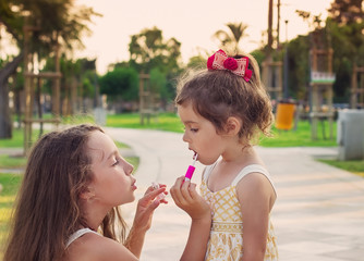 Outdoor portrait of Little beautiful girls painting lips of pink lipstick