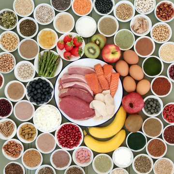 Large health food selection for body builders with meat, salmon, dairy, fruit, nuts, pulses, seeds, cereals  and supplement powders forming a background.