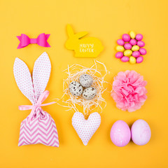 Flat lay stylish set: pink and yellow Easter eggs, fabric bunny gift bags with candies and decoration
