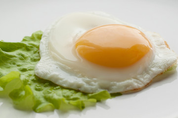 sunny side up eggs from one egg with green leaf lettuce on a white plate