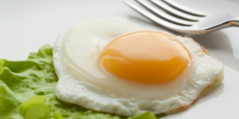 sunny side up eggs from one egg with green leaf lettuce on a white plate