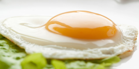 sunny side up eggs from one egg with green leaf lettuce on a white plate