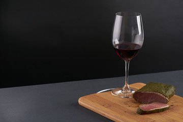 Smoked meat.Spicy bacon and glass of red wine  on wooden cutting board.Black background.Copy spase.