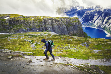 Hiker with backpack walking in Norway mountains by trail to Trolltunga nature attraction.. Fitness and healthy lifestyle outdoors.