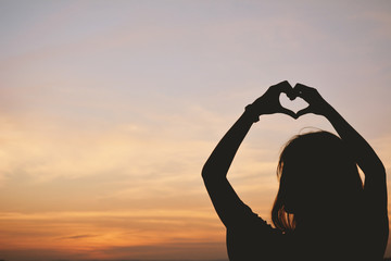 Silhouette hand of women in the heart shape at the sky sunset ba
