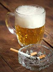 Burning cigarette in a glass ashtray and mug of beer