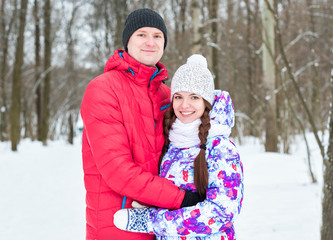 Fototapeta na wymiar Embracing couple looking at camera with smiles in winter park