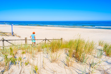 Young woman standing by wooden fence of entrance to beautiful Lubiatowo beach, Baltic Sea, Poland