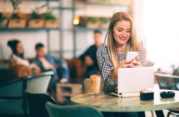 Young gorgeous woman having smart phone conversation while sitting in front of open laptop computer in cafe bar