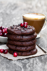 Stack  of dark chocolate cookies with cranberry and cup of coffe