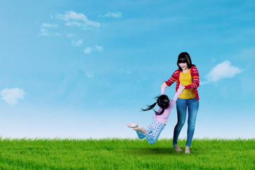 Young mother swings her daughter on meadow