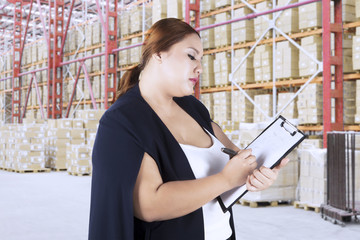 Young woman making goods list in warehouse