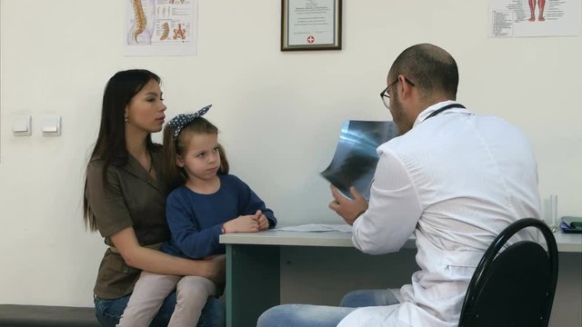 Doctor explaining chest xray image to mother holding little daughter in her arms