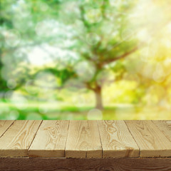 Empty wooden deck table with foliage bokeh background for product display montage. Spring or summer concept