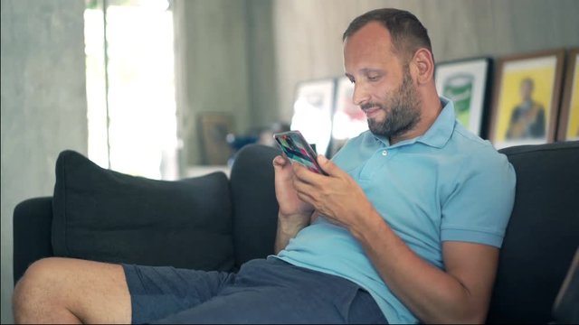 Young man using smartphone sitting on sofa, 4K
