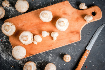 Fresh raw mushroom champignon on a cutting board, with a knife. On a dark gray stone table. Top view