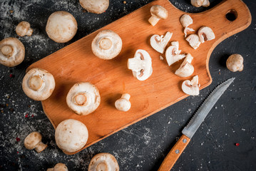 Fresh raw mushroom champignon on a cutting board, with a knife. On a dark gray stone table. Top view