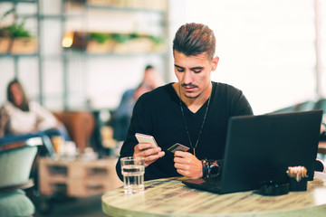 Young man working on laptop while sitting at cafe and using credit card