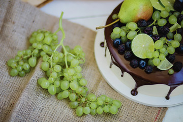Cake under the chocolate icing, decorated with pear, grapes and lime. Burlap, twine and kraft paper in the background.