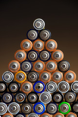 Many different colored AA batteries arranged in a pyramid on a dark gradient background 