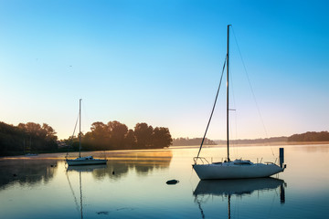 Yachts float on the calm waters of the lake. Early morning. Masuria, Poland . - obrazy, fototapety, plakaty