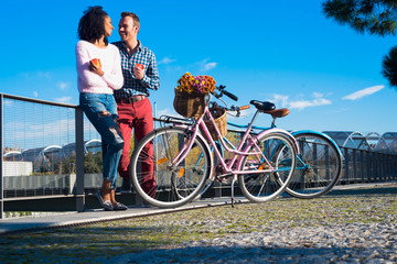 Obraz premium Happy interracial couple by the river with their vintage bycicle