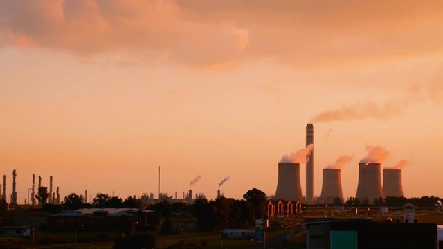 Industrial sunset skyline of cement chimneys constantly smoking from coal burning chemical engineering petroleum plant. Flames consume expelled toxic gas