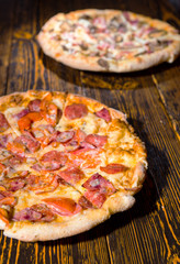 Two different pizzas with variety of toppings and cheese