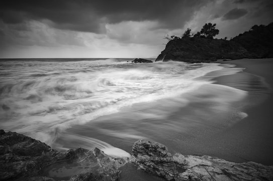 black and white image,soft wave flow hitting the sandy beach over dark cloud background. soft focus image due to long exposure shot