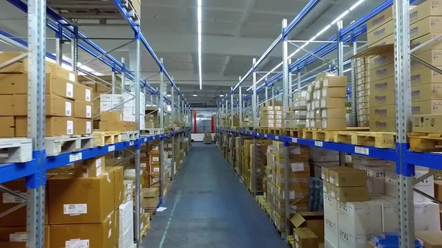 Camera moves between shelves with cardboard boxes in storage warehouse HD video. Logistics stock interior