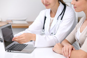  Close up of a doctor and  patient  sitting at the desk. Physician pointing into laptop computer. Medicine and health care concept
