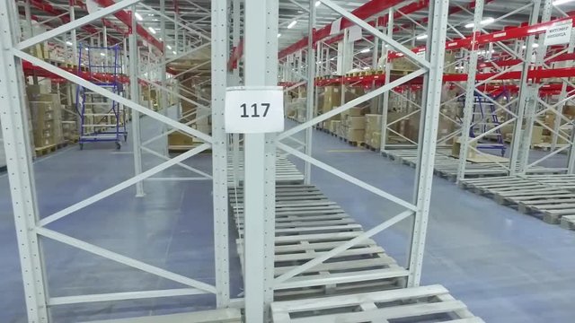 Camera moves past shelves with cardboard boxes in storage warehouse HD video. Logistics stock indoor interior