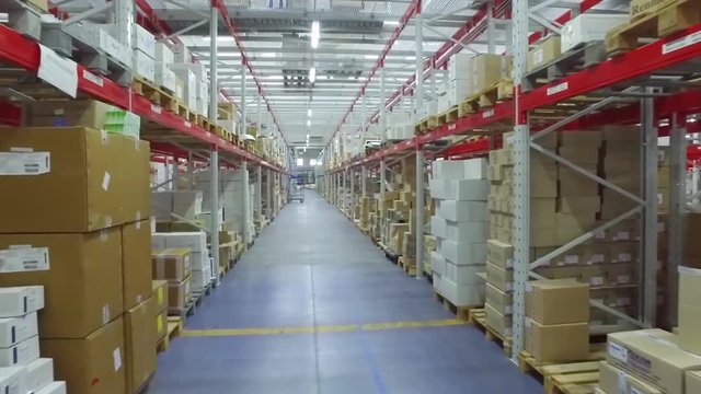 Camera moves between shelves with cardboard boxes in storage warehouse HD video. Logistics stock interior