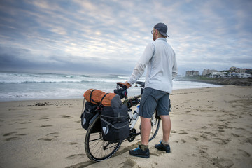 Young man with packed bicycle on beach
