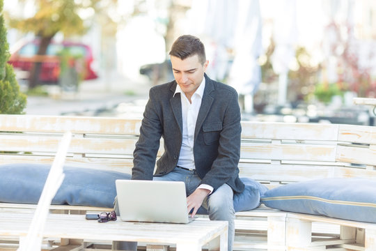 Handsome young businessman is sitting in the outdoor café and working on laptop.