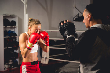 Woman boxer hitting training mitts held by her coach