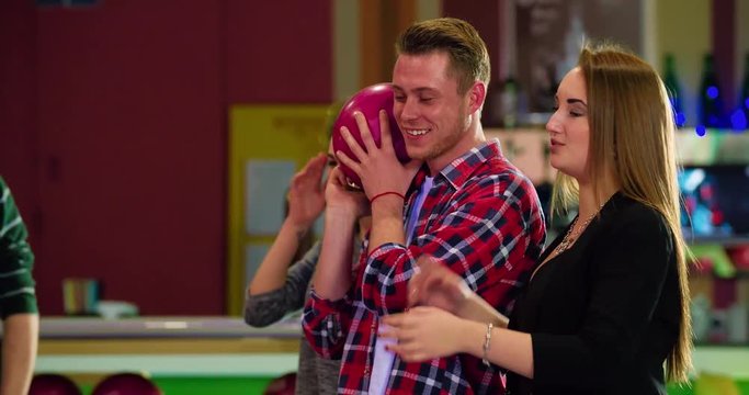Friends playing and having fun at bowling 4k leisure video. Young man holds the ball, prepares for rolling. Game players talking and laughing