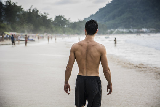 Half body back shot of a handsome young man standing on a beach in Phuket Island, Thailand, shirtless wearing boxer shorts, showing muscular fit body