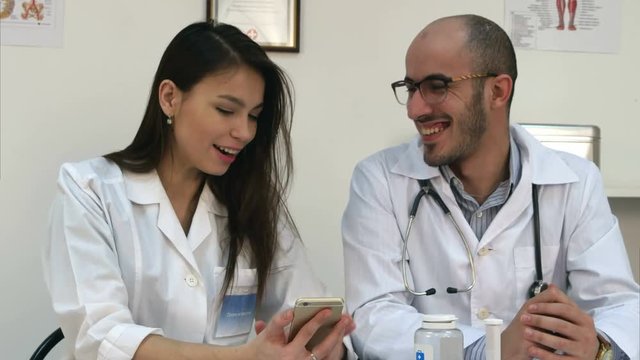Pretty young nurse showing something funny on her phone to male colleague